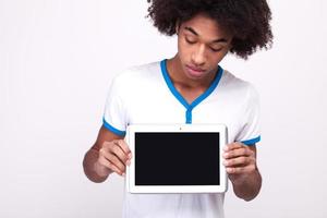 Looking at copy space. Curious African teenager on touchscreen of digital tablet while standing isolated on grey background photo