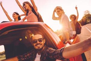 Capturing bright moments. Group of young cheerful people having fun in pick-up truck while driver making selfie photo