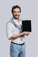 Convinient way of connection. Beautiful young man in smart casual clothes holding digital tablet and smiling while standing against grey background photo