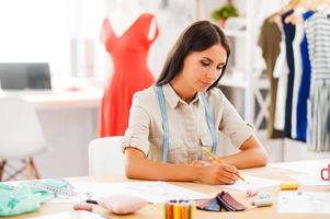 diseñador de moda en el trabajo. mujer joven seria dibujando mientras se sienta en su lugar de trabajo en el taller de moda foto