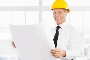 I have a plan. Confident senior man in formalwear and hardhat holding a blueprint and smiling at camera photo