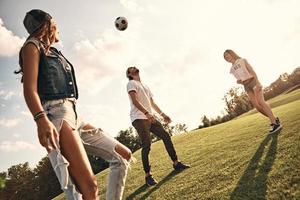 Group of young smiling people in casual wear playing soccer while standing outdoors photo