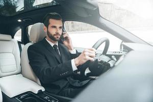 Important phone talk. Handsome young businessman talking on his smart phone with serious face while driving the car photo