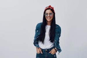 Attractive young woman in bandana looking at camera and smiling while standing against grey background photo