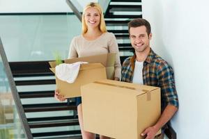 felices propietarios de la nueva casa. alegre pareja joven sosteniendo cajas de cartón mientras está de pie en las escaleras de su nueva casa foto