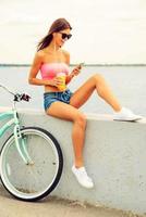 pasar tiempo sin preocupaciones al aire libre. bella joven sonriente con auriculares sentada en el parapeto cerca de su bicicleta y escuchando música foto