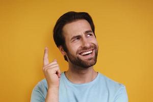 Portrait of happy young man in casual clothing gesturing and looking away while standing against yellow background photo
