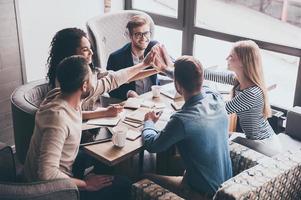 This is our success Cheerful young people giving each other high-five with smile while sitting at the office table on business meeting photo