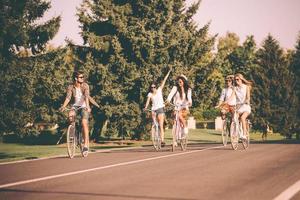 pasar un buen rato con amigos. grupo de jóvenes montando en bicicleta a lo largo de una carretera y luciendo felices foto