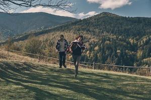 se siente como volar. Longitud total de feliz pareja joven sonriendo mientras corre en el valle en las montañas al aire libre foto