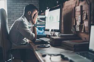 Stressful day at the office. Young businessman holding hands on his face while sitting at the desk in creative office photo