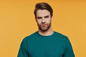 Portrait of frustrated young man looking at camera while standing against yellow background photo