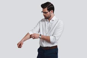 Taking everything seriously. Good looking young man in formalwear adjusting his sleeve while standing against grey background photo