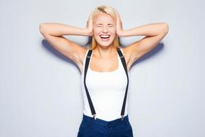 I refuse to hear you. Surprised young woman covering ears with hand and keeping eyes closed while standing against grey background photo