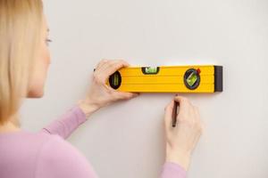 mujer con cinta métrica. vista trasera de una mujer rubia tomando medidas de la pared foto