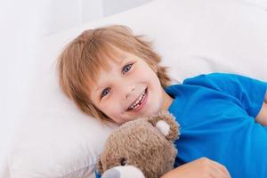 relajarse después de un largo día jugando. vista superior de un niño lindo sonriendo a la cámara mientras está acostado en la cama foto