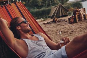 Real relaxation. Handsome young man keeping hand behind head and smiling while lying in hammock photo