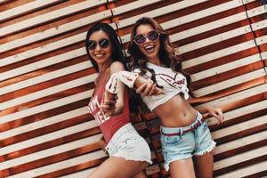 Do you want some Two attractive young women smiling and holding ice cream while standing against the wooden wall outdoors photo