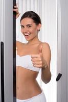 Beauty in solarium. Attractive young woman looking out of tanning booth and gesturing photo