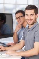 personal de TI exitoso. dos jóvenes alegres sonriendo a la cámara mientras se sientan frente a los monitores de computadora foto