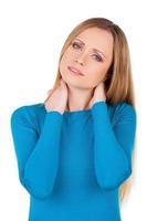 Feeling pain in a neck. Depressed young woman touching her neck and looking at camera while standing isolated on white photo