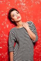 Glam and funky. Fashionable young short hair woman in striped clothing posing against red background photo