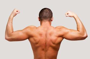 Showing his perfect muscles. Rear view of young muscular man showing his biceps while standing against grey background photo