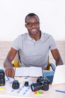 Young and creative. Top view of handsome young African man in casual wear sitting at his working place and looking at camera photo