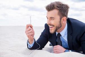 Staying connected everywhere. Happy young smiling businessman holding network cable stretching out of sand photo