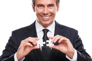 Businessman with puzzle elements. Portrait of confident mature man in formalwear holding two puzzle elements and smiling while standing against white background photo