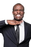 Sick and tired. Furious young African man in formalwear touching his neck with hand and grimacing while standing isolated on white background photo