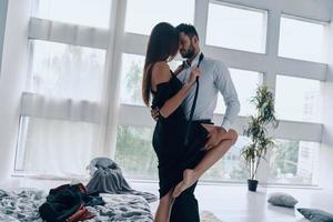 Passion. Handsome young man kissing and undressing his girlfriend while standing time in the bedroom photo