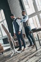 Fits perfect. Full length of young fashionable designer helping his client to get dressed while standing in his workshop photo