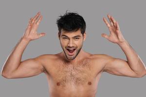 Huge surprise  Happy young man looking at camera and gesturing while standing against grey background photo