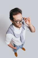 Looking for you Top view of handsome young man in smart casual clothes adjusting his eyeglasses and looking at camera while standing against grey background photo