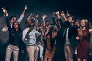 disfrutando de una fiesta increíble. grupo de hermosos jóvenes bailando con flautas de champán y luciendo felices foto