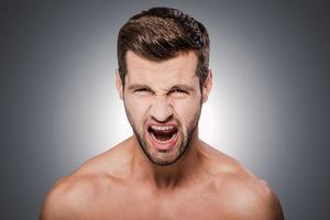 Furious man. Portrait of furious young shirtless man looking at camera and keeping mouth open while standing against grey background photo