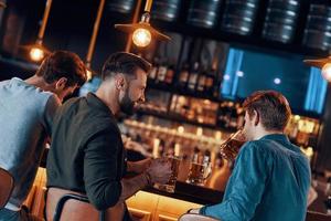 vista trasera de jóvenes felices con ropa informal disfrutando de la cerveza en el pub foto