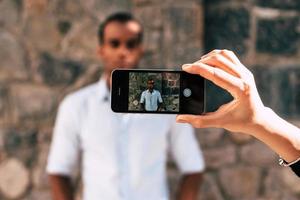 sacar una foto. mano femenina sosteniendo un teléfono inteligente y tomando una foto de un joven africano parado al aire libre