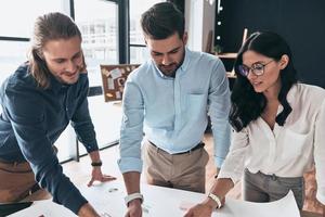 Thinking in one direction. Top view of young confident business people discussing something while pointing at blueprint in the office photo