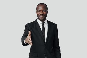 Elegant young African man in formalwear looking at camera and smiling while standing against grey background photo