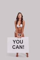 Just keep trying.  Full length of attractive young woman holding a poster and looking at camera while standing against grey background photo