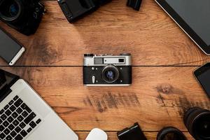 Displacement of old technology. Top view of retro camera surrounding by diverse equipment for photographer laying on the wooden grain photo