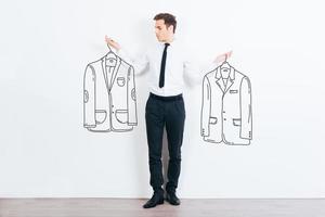 What jacket shall I choose  Handsome young man choosing between two drawn jackets while standing against white background photo