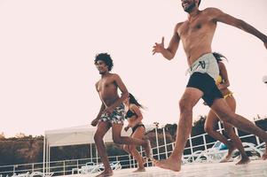 listo para refrescarse. grupo de hermosos jóvenes que se ven felices mientras se preparan para saltar a la piscina foto