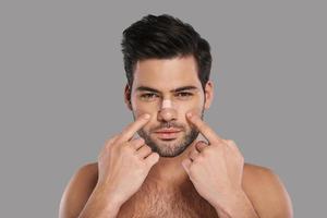 My nose Handsome young man pointing at his adhesive bandage on his nose and looking at camera while standing against grey background photo