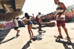 disfrutando de un tiempo sin preocupaciones juntos. grupo de jóvenes modernos patinando juntos al aire libre foto