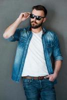 Style and confidence. Confident young man adjusting eyewear and looking away while standing against grey background photo