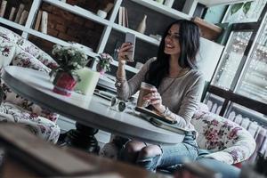 recibiendo lindos mensajes. atractiva joven mujer sonriente usando su teléfono inteligente mientras está sentada en el restaurante foto