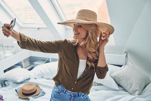 Beautiful young smiling woman making selfie while sitting in bed at home photo